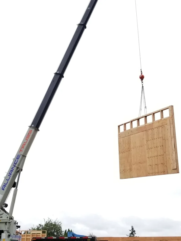 Large industrial crane lifting a wooden crate onto a flatbed truck at a loading facility.