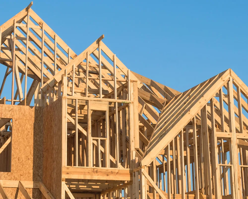Wooden frame house structure under construction against clear blue sky.