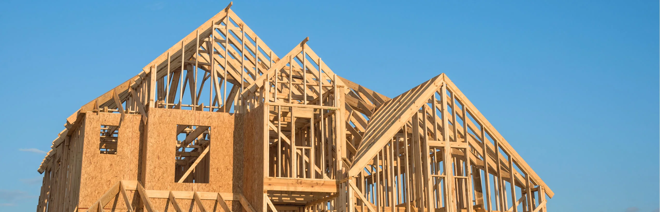 Wooden frame house structure under construction against clear blue sky.