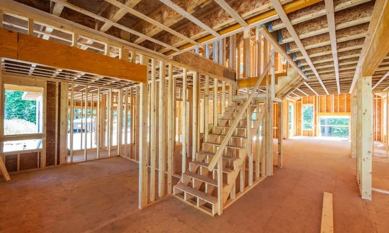 Interior framing of a residential home under construction showing wooden studs, doorways, and staircase structure.