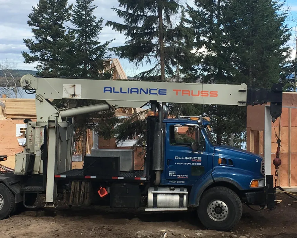 Crane truck with aerial lift parked at a job site with wooden structures in background.