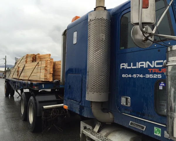 Blue Alliance semi-truck with flatbed trailer carrying wooden pallets on a highway