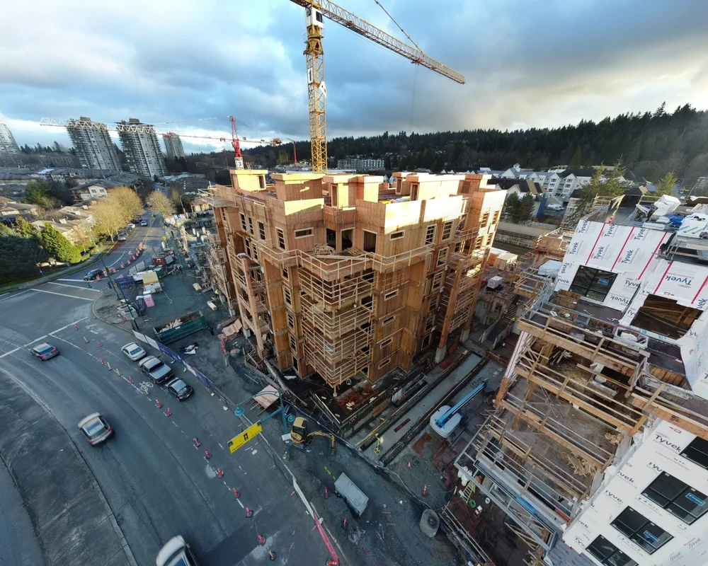 A brick apartment building under construction with a yellow crane on an urban street corner.