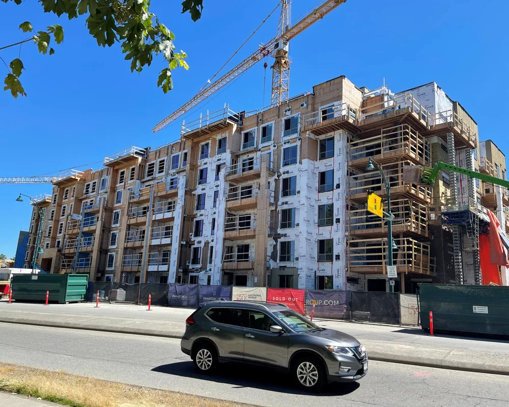 Multi-story residential building under construction with crane and scaffolding on urban street.