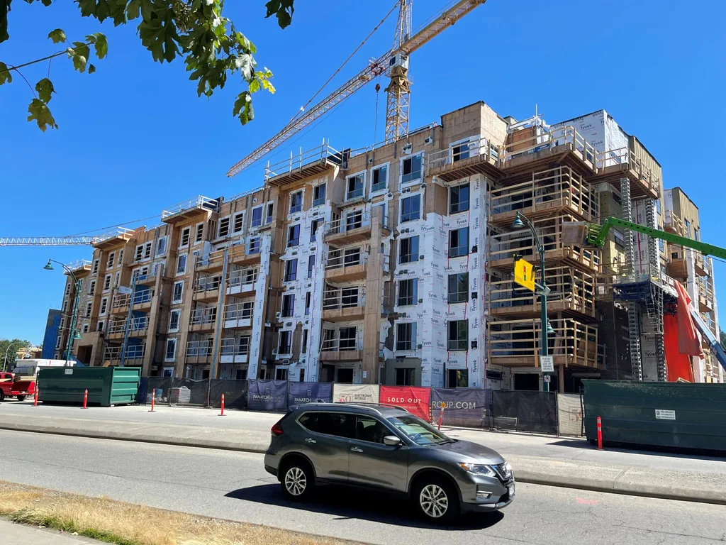 Multi-story residential building under construction with crane and scaffolding on urban street.
